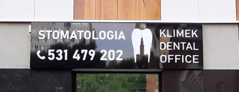 Czarny podłużny kaseton z błyszczącego dibondu i białą płaską grafiką stomatologia