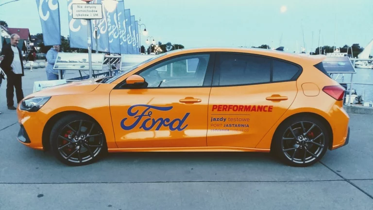 Grafika promocyjno-informacyjna na pomarańczowym samochodzie marki Ford Focus