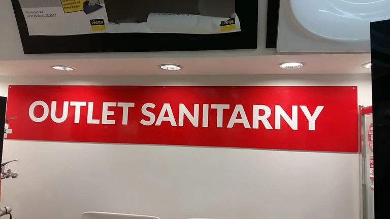 Podłużna tablica z czerwonego dibondu z napisem outlet sanitarny w firmie kim. szyldy reklamowe warszawa